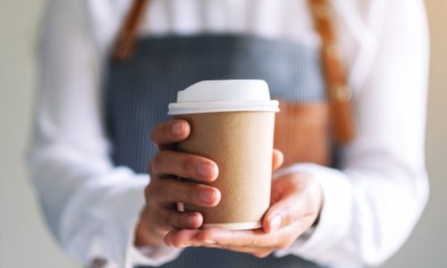 A waitress holding and serving a paper cup of hot coffee in cafe