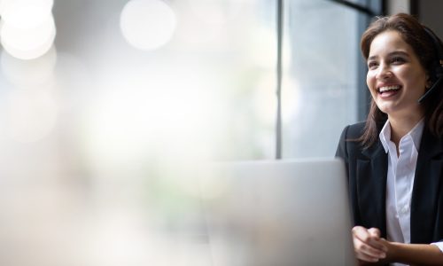 Attractive business woman Asian in suits and headsets are smiling while working with computer at office. Customer service assistant working in office. VOIP Helpdesk headset